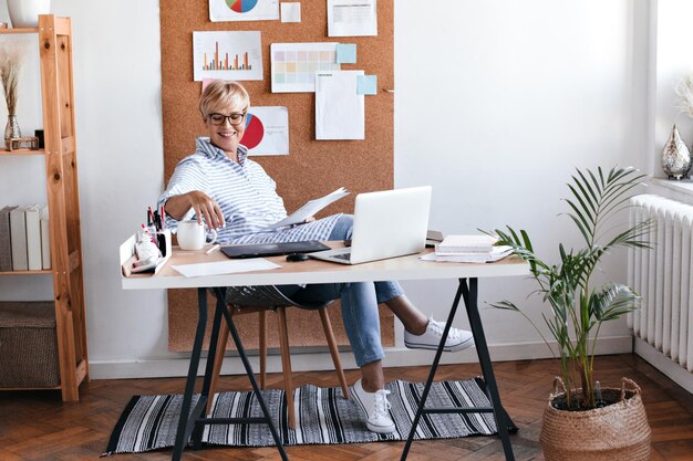 Charmante Dame in blauem Outfit, die im Büro sitzt und Kaffee genießt