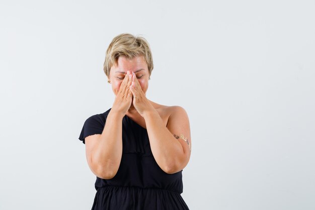 Charmante Dame in der schwarzen Bluse, die Gesicht mit Händen hält und emotional schaut