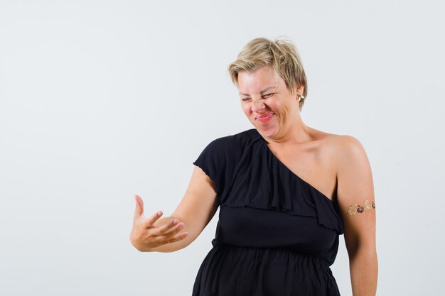 Charmante Dame in der schwarzen Bluse, die wie schauendes Foto am Telefon aufwirft und optimistisch schaut