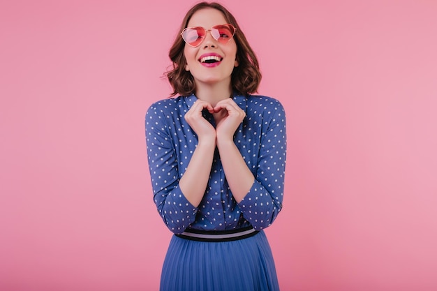 Charmante europäische junge Frau in blauer Bluse, die auf pastellfarbenem Hintergrund lacht Begeistertes weißes Mädchen mit Sonnenbrille, das Spaß hat, während es im Studio posiert