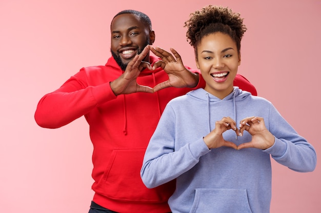 Charmante freudige fürsorgliche junge afroamerikanische Familienvater Frau Geschwister, die breit lächeln, zeigen Herzgesten, die grinsen Liebe Empathie Positivität ausdrücken, zwei treue Freunde schätzen Freundschaft