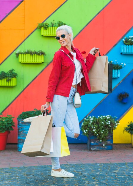 Charmante junge Frau mit Taschen in der Nähe von Wand