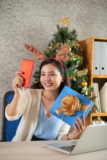 Charmante schöne Geschäftsfrau, die mit Weihnachtsgeschenk lächelt und fotografiert
