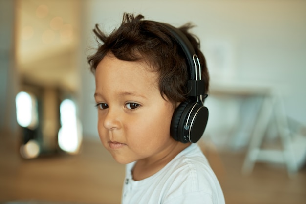 charmanter süßer kleiner Junge mit lockigem Haar drinnen mit kabellosem Headset