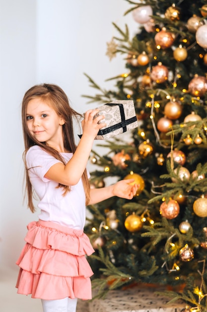 Charmantes kleines Mädchen hält ein Geschenk auf einem Hintergrund von Weihnachtsbäumen