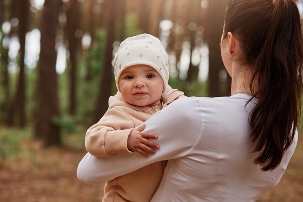 Charmantes süßes kleines Baby in Mamas Händen, das nach vorne schaut