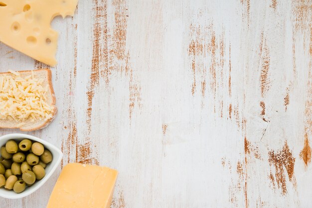 Cheddarkäsekäse mit grünen Oliven auf weißem Holztisch