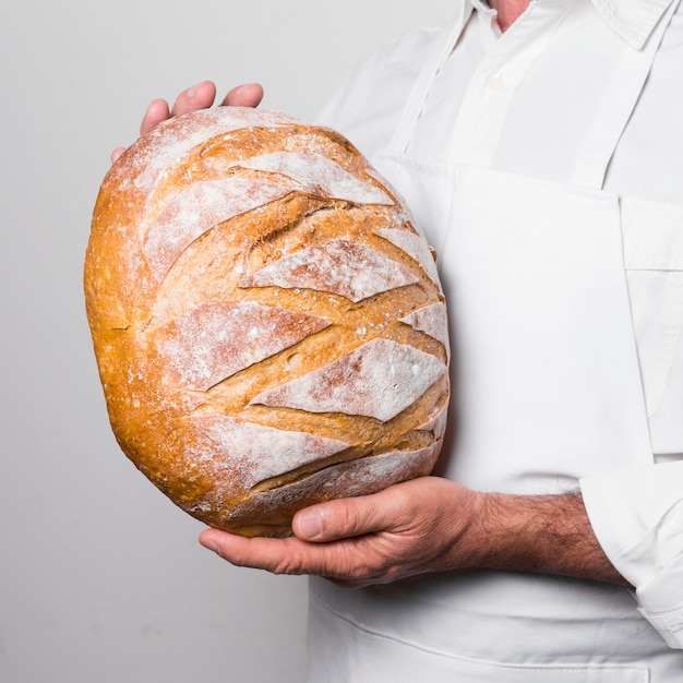 Chef, der weiße Kleidung trägt, die ein warmes Brot hält