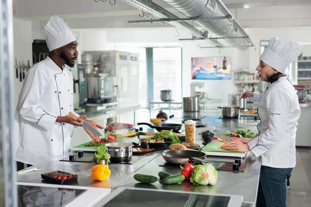 Chef- und Sous-Chef diskutieren darüber, welches Rezept für das Abendessen in einem gehobenen Restaurant zubereitet werden soll. Erfahrene Gastronomieexperten kochen in der professionellen Küche Gourmetgerichte.