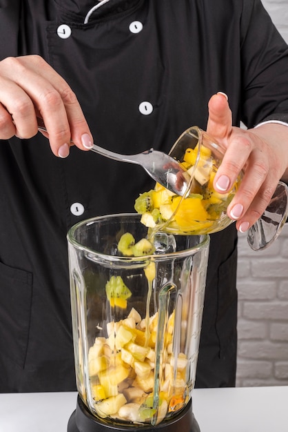 Kostenloses Foto chefkoch, der dem mixer früchte hinzufügt