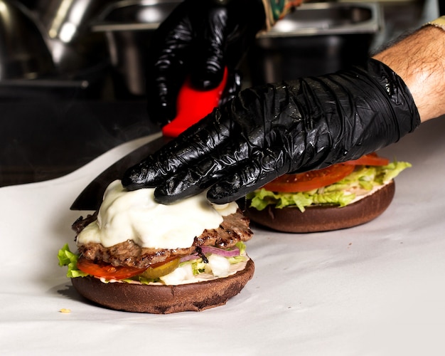 Chefkoch in schwarzen Handschuhen bereitet Rindfleischburger zu
