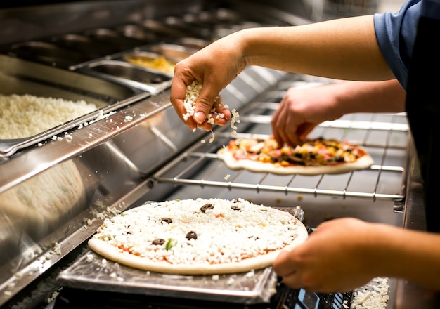 Chefkoch legt Käse auf Pizzateig mit Tomatensauce bedeckt