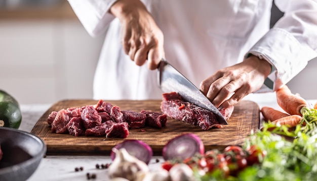 Chefkoch schneidet rotes fleisch in kleine stücke, um eintopf oder gulasch zuzubereiten.