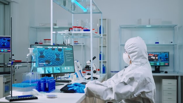 Chemiker tippen auf PC und Mitarbeiter analysieren Objektträger im ausgestatteten Labor. Wissenschaftlerteam, das die Entwicklung von Impfstoffen mit Hightech untersucht, um die Behandlung gegen das Covid19-Virus zu erforschen