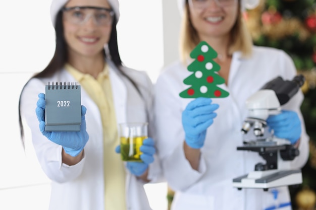 Chemikerinnen, die mikroskop und kalender für 2022 in der nähe von neujahrsbaum in der nähe halten