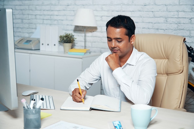 Chest-up schoss vom Büroangestellten, der am Schreibtisch sitzt und Kenntnisse nimmt