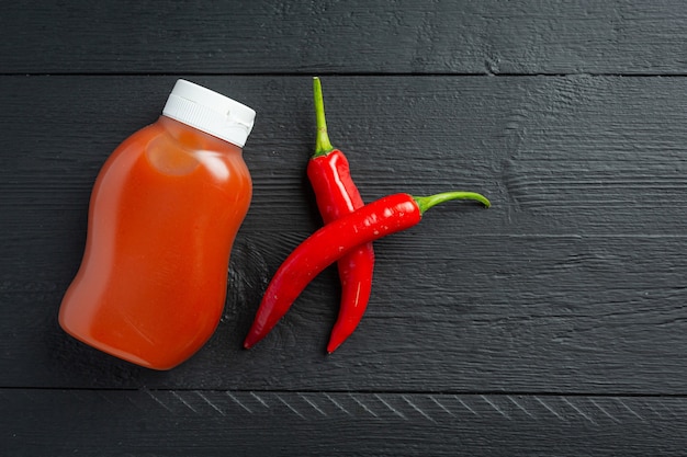 Chilisauce in Flasche und Paprika auf dunkler Holzoberfläche