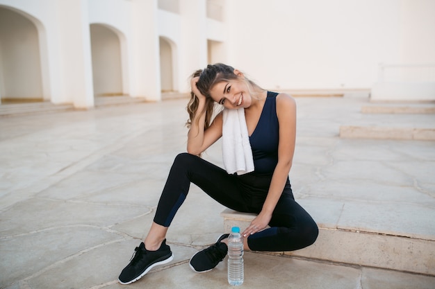 Chillen der attraktiven jungen Frau in der Sportbekleidung auf ostweißer Architektur. Resort, Training, fröhliche Stimmung, Lächeln, Ausdruck wahrer positiver Emotionen