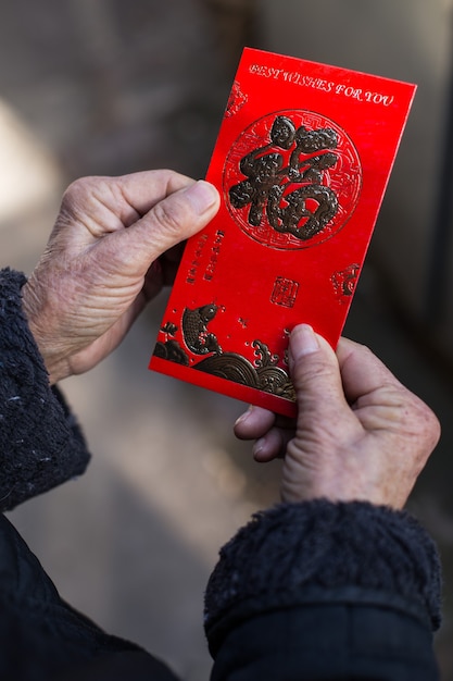 Chinesische Frau, die einen traditionellen roten Umschlag mit chinesischen Neujahrswünschen hält