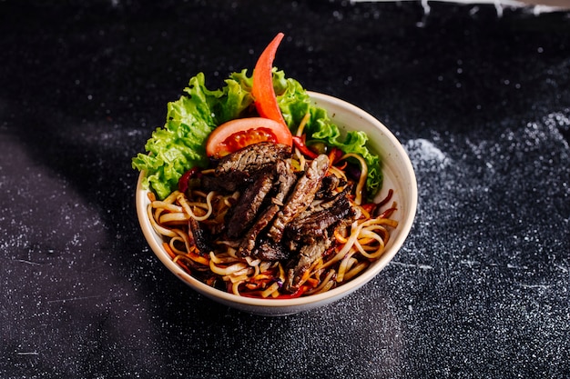 Chinesische Nudeln in Schüssel mit gehacktem Steak, Tomatenscheiben und Salat.