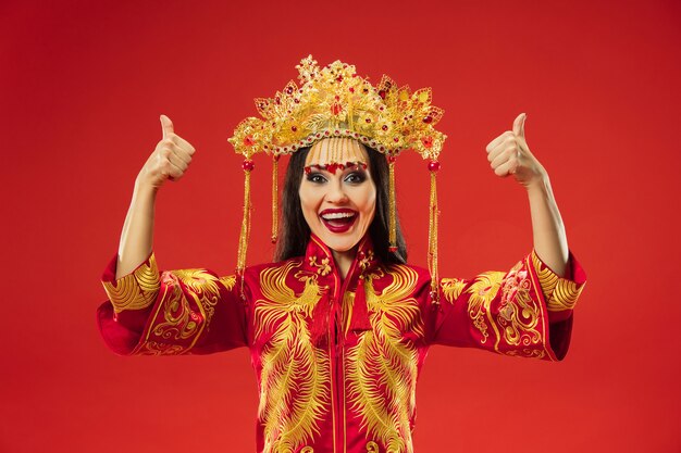 Chinesische traditionelle anmutige Frau im Studio über rotem Hintergrund. Schönes Mädchen, das Nationaltracht trägt. Chinesisches Neujahr, Eleganz, Anmut, Darsteller, Performance, Tanz, Schauspielerin, Emotionskonzept