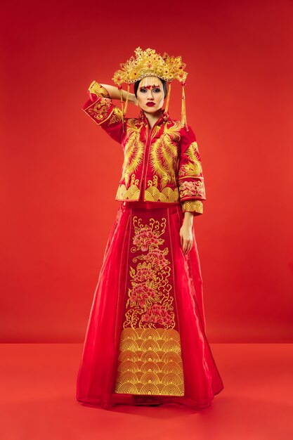 Chinesische traditionelle anmutige Frau im Studio über rotem Hintergrund. Schönes Mädchen, das Nationaltracht trägt. Chinesisches Neujahr, Eleganz, Anmut, Darsteller, Performance, Tanz, Schauspielerin, Emotionskonzept