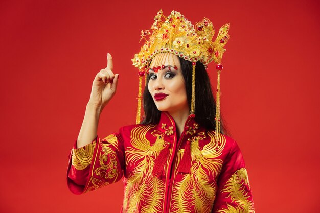 Chinesische traditionelle anmutige Frau im Studio über rotem Hintergrund. Schönes Mädchen, das Nationaltracht trägt. Chinesisches Neujahr, Eleganz, Anmut, Darsteller, Performance, Tanz, Schauspielerin, Emotionskonzept