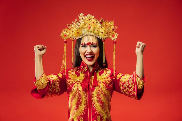 Chinesische traditionelle anmutige Frau im Studio über rotem Hintergrund. Schönes Mädchen, das Nationaltracht trägt. Chinesisches Neujahr, Eleganz, Anmut, Darsteller, Performance, Tanz, Schauspielerin, Kleidungskonzept