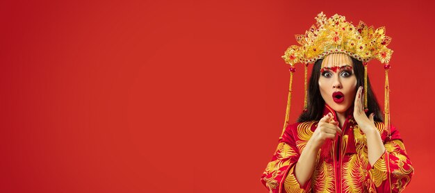 Chinesische traditionelle anmutige Frau im Studio über rotem Hintergrund. Schönes Mädchen, das Nationaltracht trägt. Chinesisches Neujahr, Eleganz, Anmut, Darsteller, Performance, Tanz, Schauspielerin, Kleidungskonzept