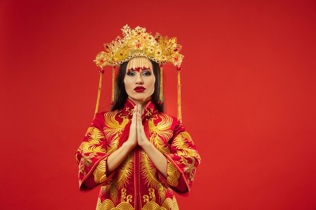 Chinesische traditionelle anmutige Frau im Studio über rotem Hintergrund. Schönes Mädchen, das Nationaltracht trägt. Chinesisches Neujahr, Eleganz, Anmut, Darsteller, Performance, Tanz, Schauspielerin, Kleidungskonzept