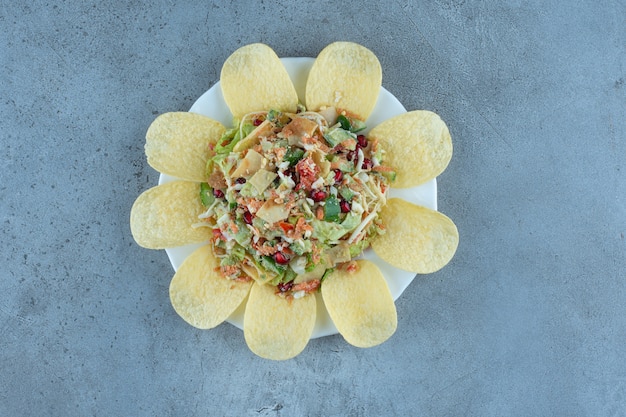 Chips, die eine portion käse- und gemüsesalat auf marmortisch umgeben.