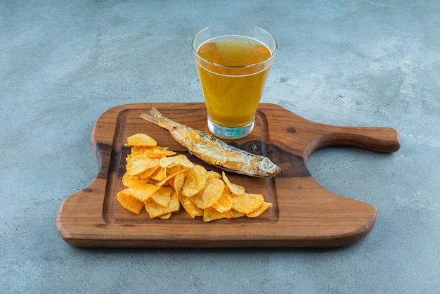 Chips, Fisch und Glas Bier auf einem Brett, auf dem Marmorhintergrund.