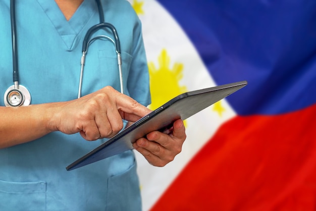 Chirurg oder arzt, der ein digitales tablett auf dem hintergrund der philippinischen flagge verwendet