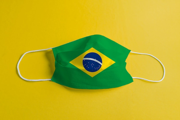 Chirurgische maske auf gelbem hintergrund mit brasilianischer flagge