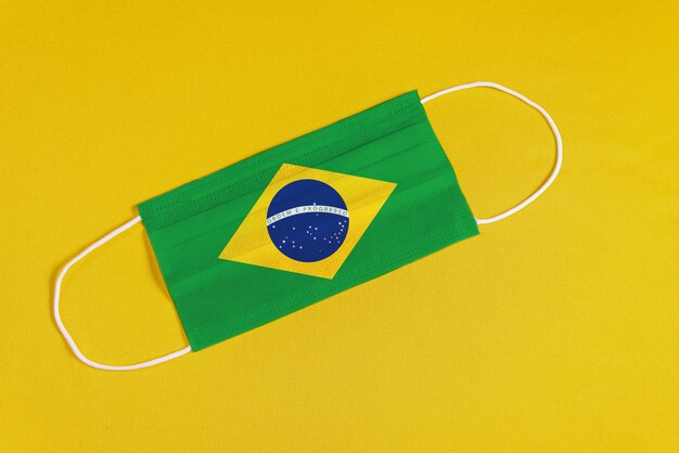 Chirurgische Maske auf gelbem Hintergrund mit brasilianischer Flagge