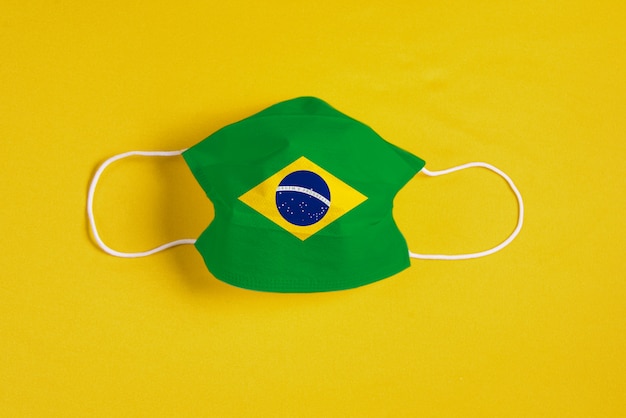 Chirurgische Maske auf gelbem Hintergrund mit brasilianischer Flagge