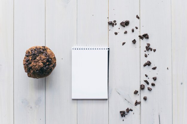 Choco-Chip-kleiner Kuchen mit gewundenem Notizblock und zerstreute Schokolade auf hölzerner Planke