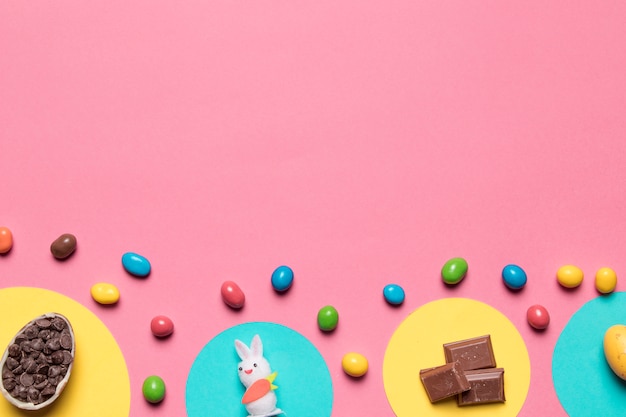Choco-Chips; Kaninchen-Statue; Schokoladenstücke und bunte Süßigkeiten auf rosa Hintergrund mit Platz für Text