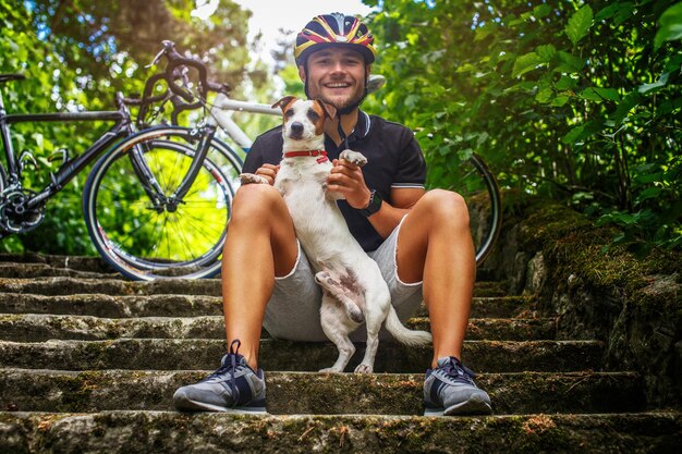 Ciclist-Männchen posiert mit seinem Russel-Hund auf Treppen in einem Wald.