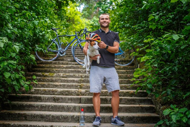 Ciclist-Männchen posiert mit seinem Russel-Hund auf Treppen in einem Wald.