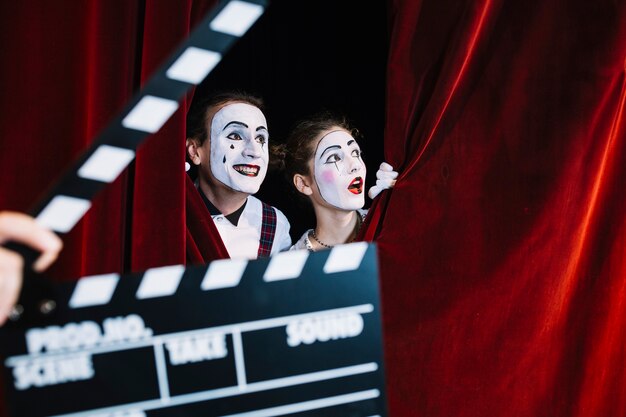 Clapperboard vor den aufgeregten Pantomimepaaren, die hinter den roten Vorhang spähen