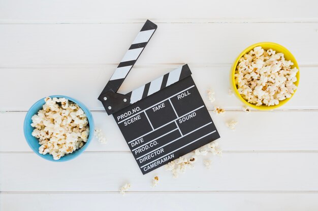 Clapperboard zwischen Schüsseln Popcorn