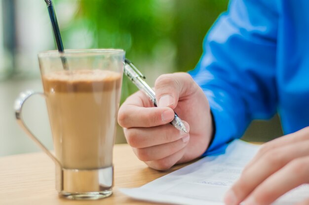 Close-up Geschäftsmann sitzt am Tisch im Büro Interieur und aufmerksam schriftlich einige Notizen. Kaffee auf dem Tisch.