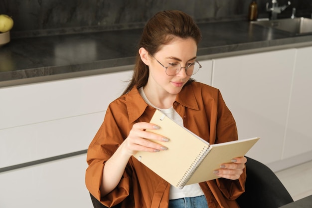 Kostenloses Foto close-up-porträt einer jungen studentin in der küche mit einem notizbuch, die zu hause für die prüfung überarbeitet