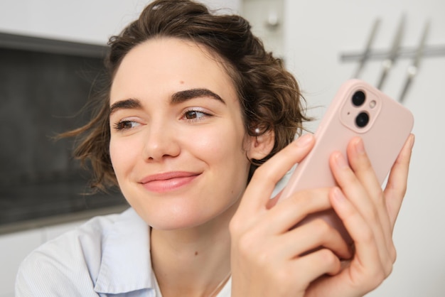 Close-up-Porträt einer lächelnden brünetten Frau mit einem Smartphone, die ein Handy in der Hand hält und sieht aus