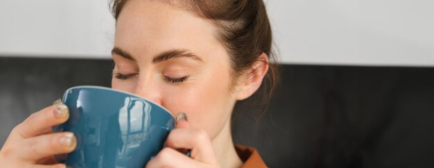 Kostenloses Foto close-up-porträt einer schönen, entspannten jungen frau, die das aroma von kaffee, cappuccino und