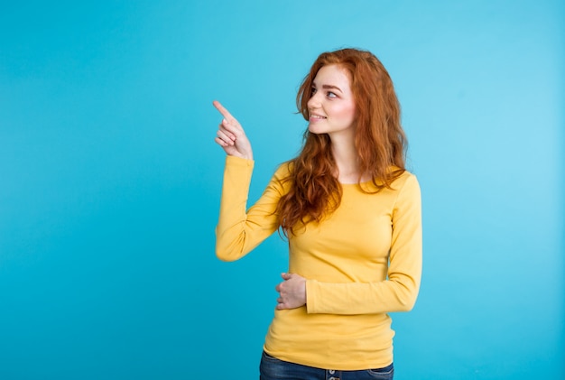 Close up Portrait junge schöne attraktive Redhair Mädchen glücklich mit etwas und zeigt Finger. Blauer Pastellhintergrund. Platz kopieren