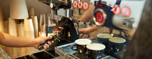 Kostenloses Foto close-up von barista-hand und kaffeemaschine mit frischen gemahlenen bohnen in einem café