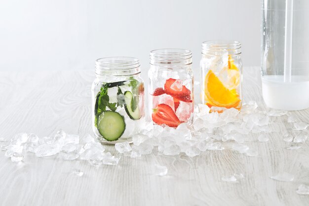 Closeup Gläser mit Eis und verschiedenen Füllungen Orange, Erdbeere, Gurke und Minze zubereitet, um frische hausgemachte Limonade mit Sprudelwasser zu machen