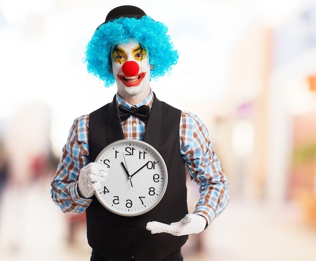 Clown mit blauen Perücke zeigt eine Uhr